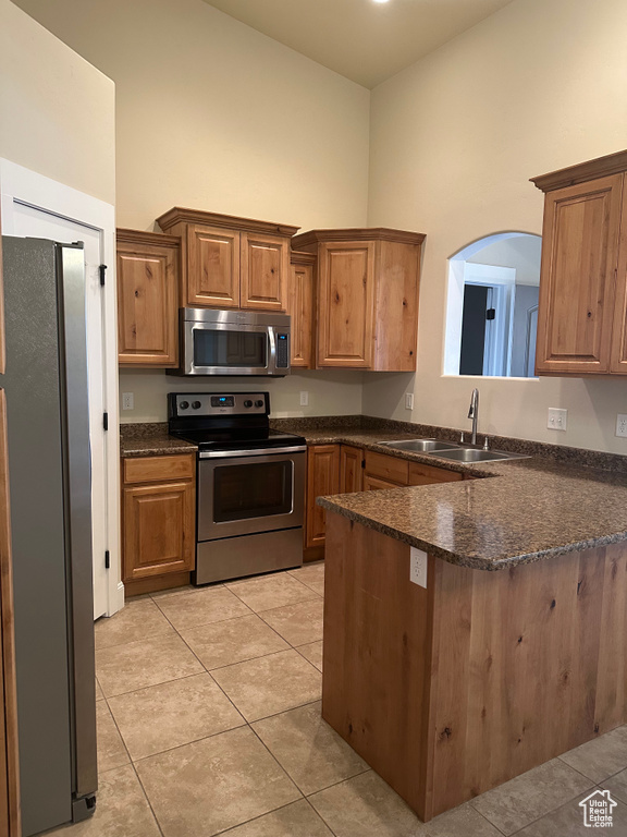 Kitchen featuring stainless steel appliances, a sink, a towering ceiling, a peninsula, and light tile patterned flooring
