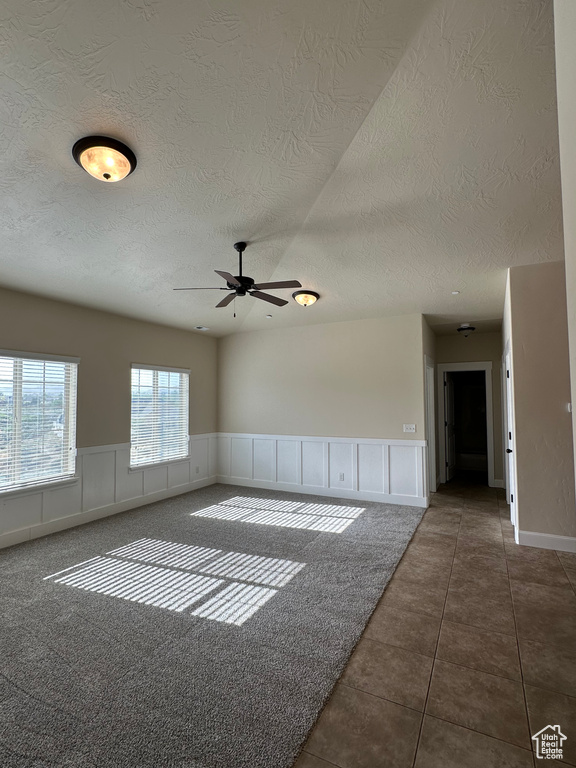 Spare room featuring a textured ceiling, a ceiling fan, wainscoting, and tile patterned flooring