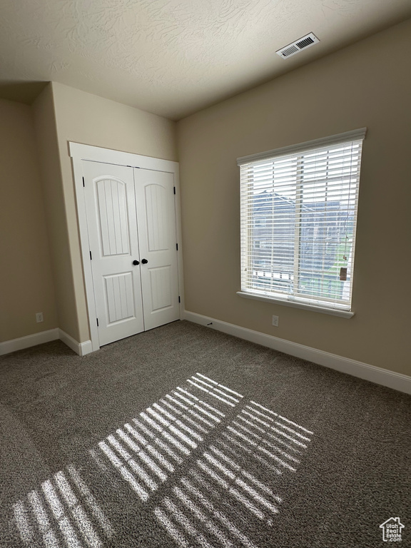 Unfurnished bedroom with baseboards, carpet floors, a closet, and a textured ceiling