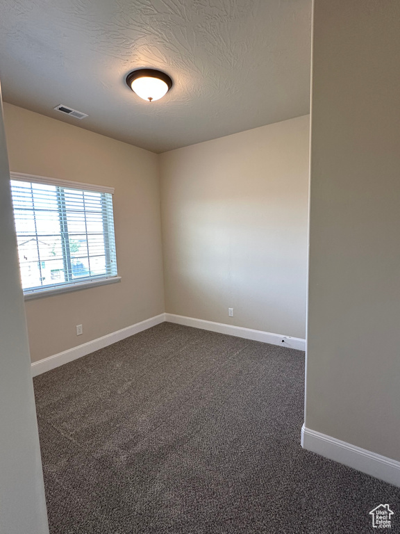 Unfurnished room with dark carpet, baseboards, and a textured ceiling