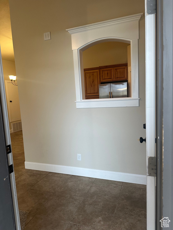 Empty room with baseboards, dark tile patterned flooring, and arched walkways