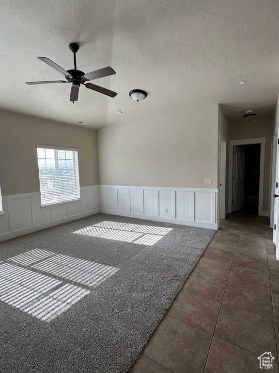Tiled spare room with a textured ceiling, ceiling fan, a decorative wall, and a wainscoted wall