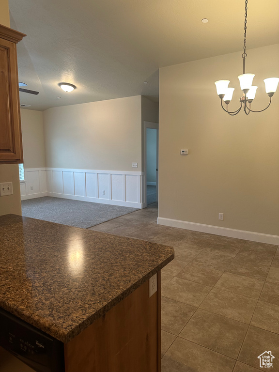 Kitchen with stainless steel dishwasher, wainscoting, a chandelier, dark tile patterned flooring, and decorative light fixtures