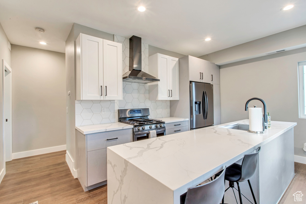 Kitchen with stainless steel appliances, wall chimney range hood, a sink, baseboards, and light wood finished floors
