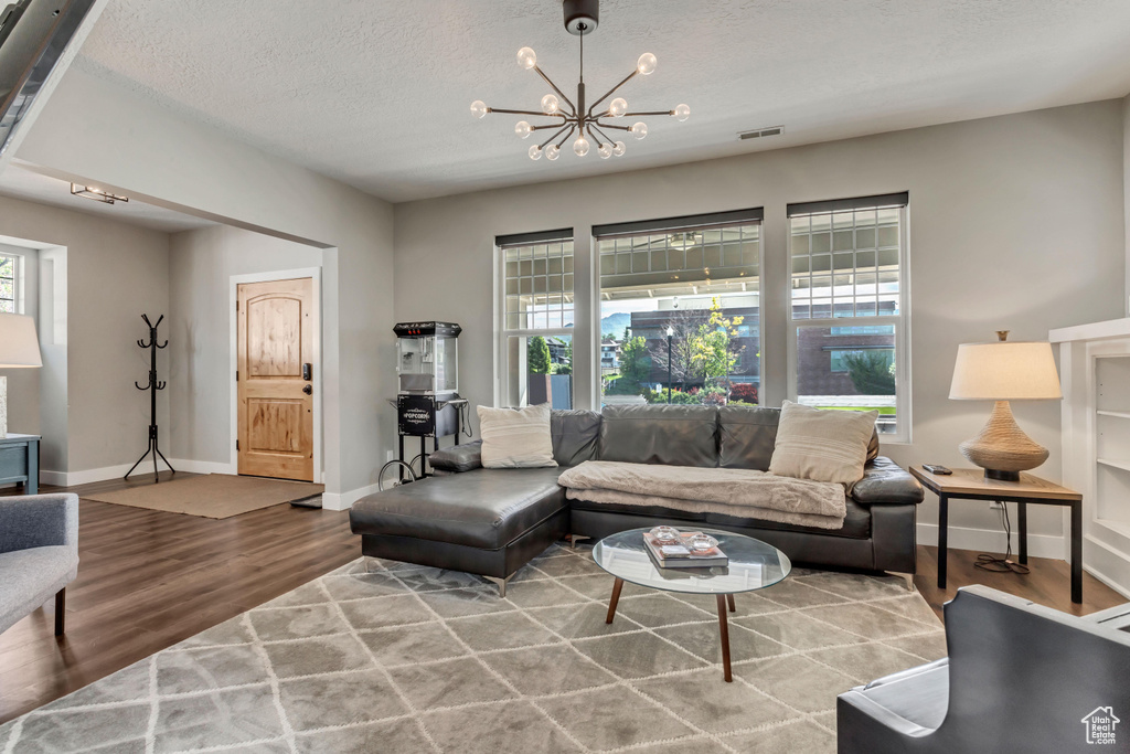 Living room featuring wood finished floors, a textured ceiling, a chandelier, baseboards, and visible vents