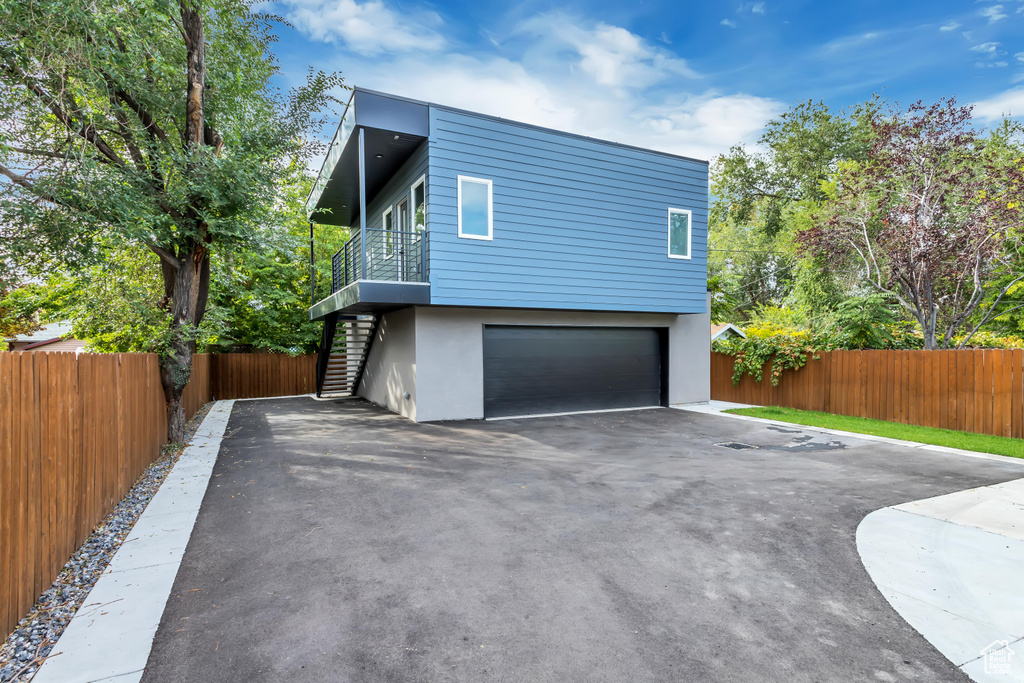 View of property exterior with stairs, an attached garage, fence, and asphalt driveway