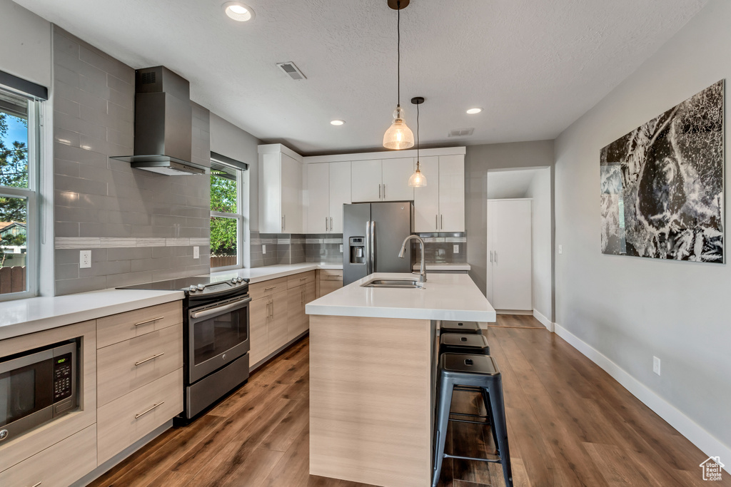 Kitchen featuring light countertops, wall chimney range hood, visible vents, a sink, and appliances with stainless steel finishes