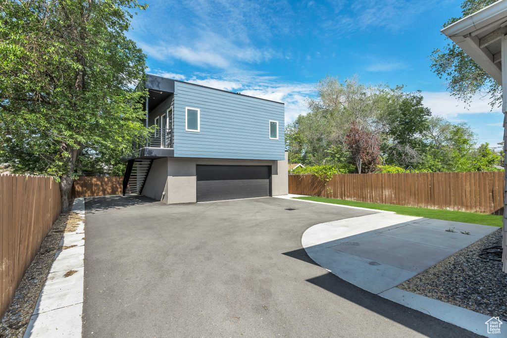 View of side of property featuring stairway, fence, stucco siding, an attached garage, and driveway