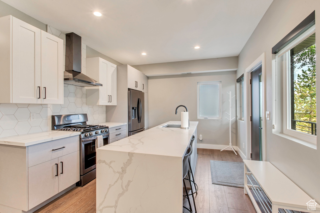 Kitchen with stainless steel appliances, wall chimney exhaust hood, a sink, white cabinetry, and recessed lighting