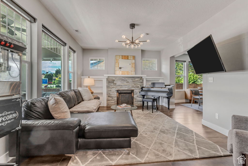 Living area with visible vents, baseboards, a notable chandelier, wood finished floors, and a stone fireplace