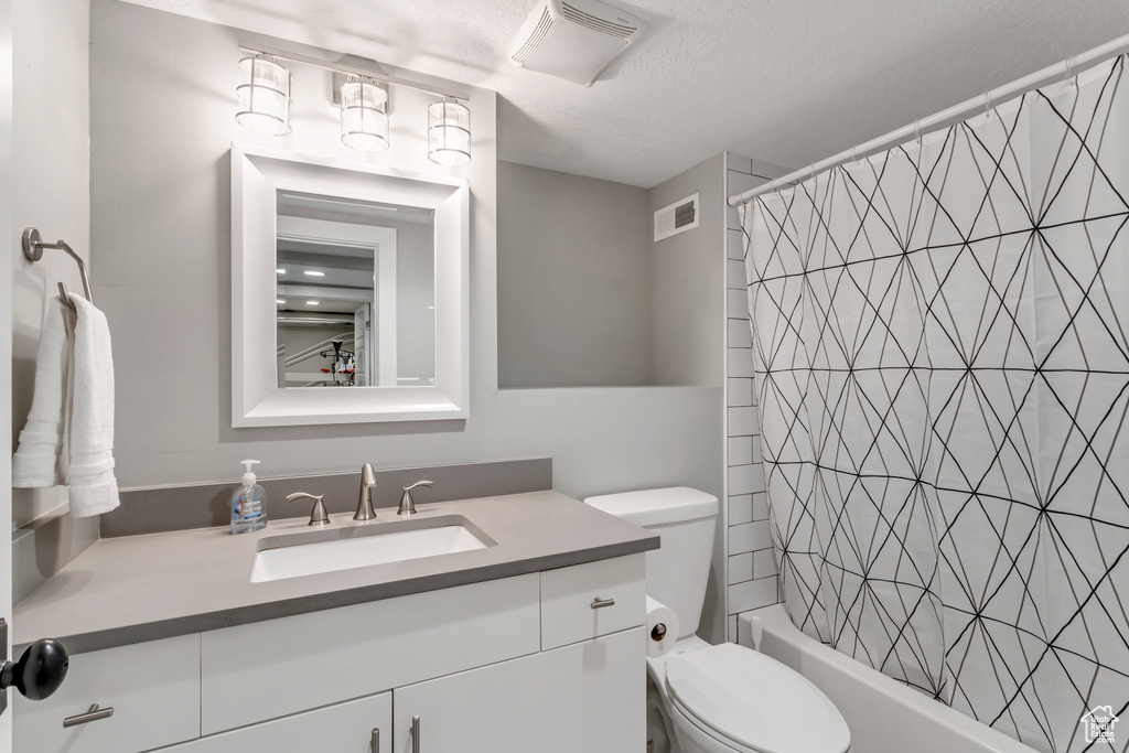 Bathroom featuring toilet, vanity, shower / bath combo, and a textured ceiling