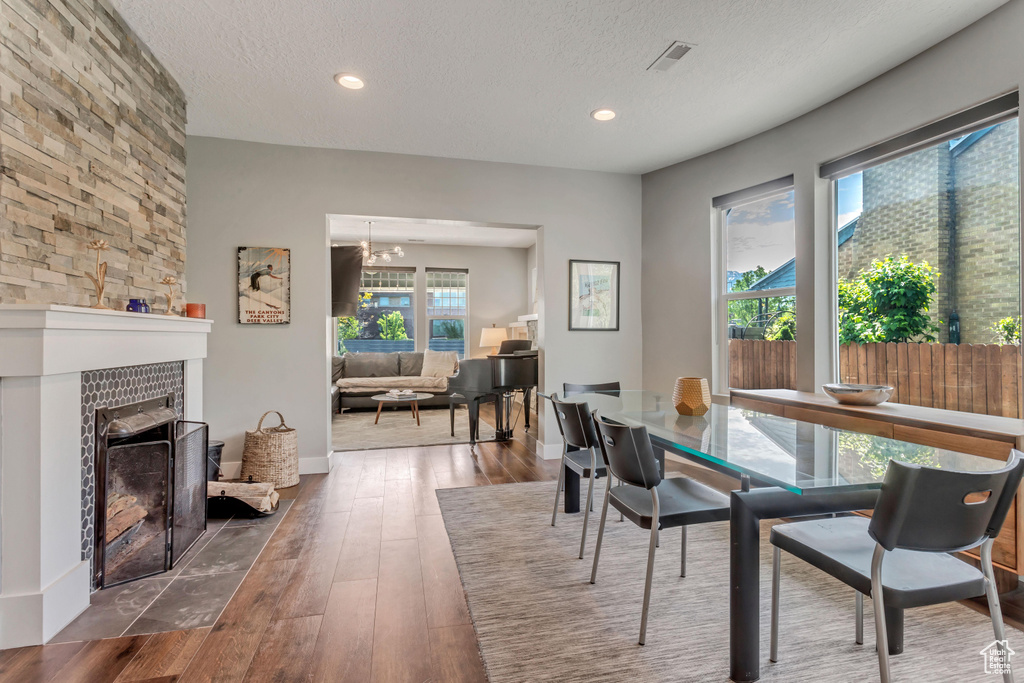 Dining area featuring a textured ceiling, hardwood / wood-style floors, recessed lighting, a tiled fireplace, and baseboards