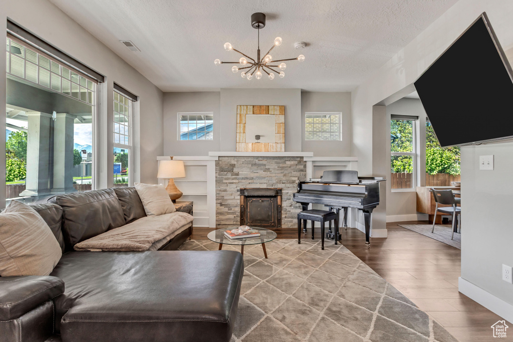 Living room with healthy amount of natural light, wood finished floors, a textured ceiling, a chandelier, and baseboards