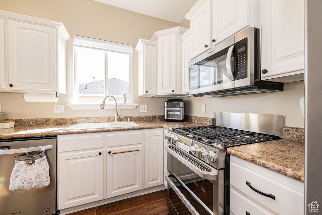 Kitchen featuring stainless steel appliances, a sink, white cabinetry, and dark wood-style floors