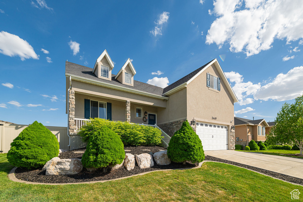View of front of home with stone siding, an attached garage, stucco siding, driveway, and covered porch