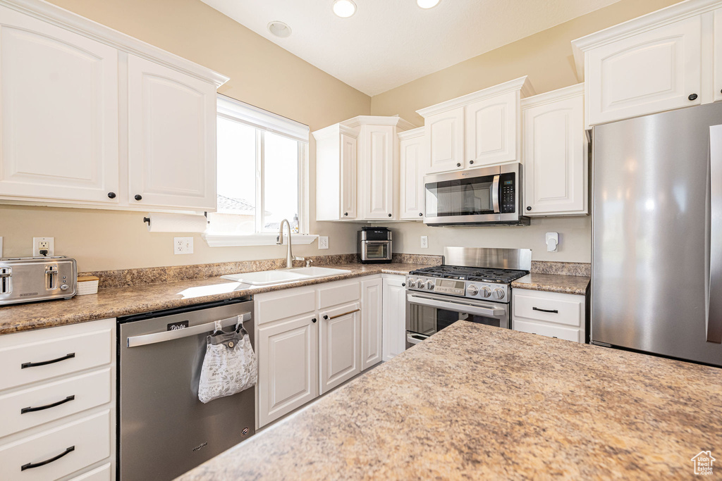 Kitchen with stainless steel appliances, a sink, white cabinets, and recessed lighting