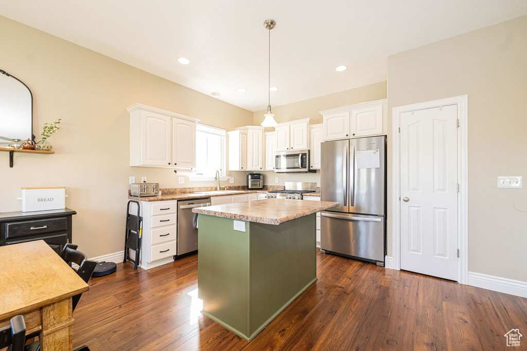 Kitchen featuring appliances with stainless steel finishes, white cabinetry, a center island, a sink, and dark wood-style floors