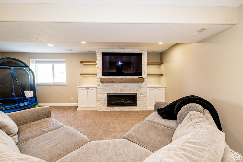 Carpeted living room featuring baseboards, a stone fireplace, and recessed lighting