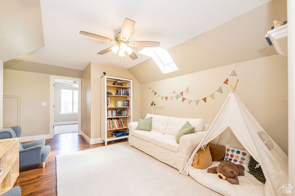 Living area with a ceiling fan, a skylight, wood finished floors, baseboards, and vaulted ceiling