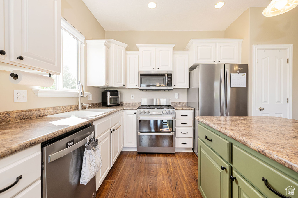 Kitchen with appliances with stainless steel finishes, a sink, green cabinetry, white cabinets, and light countertops