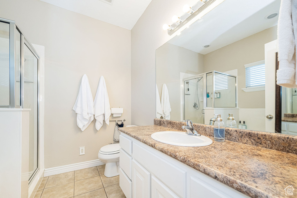Bathroom featuring a shower stall, tile patterned floors, vanity, baseboards, and toilet