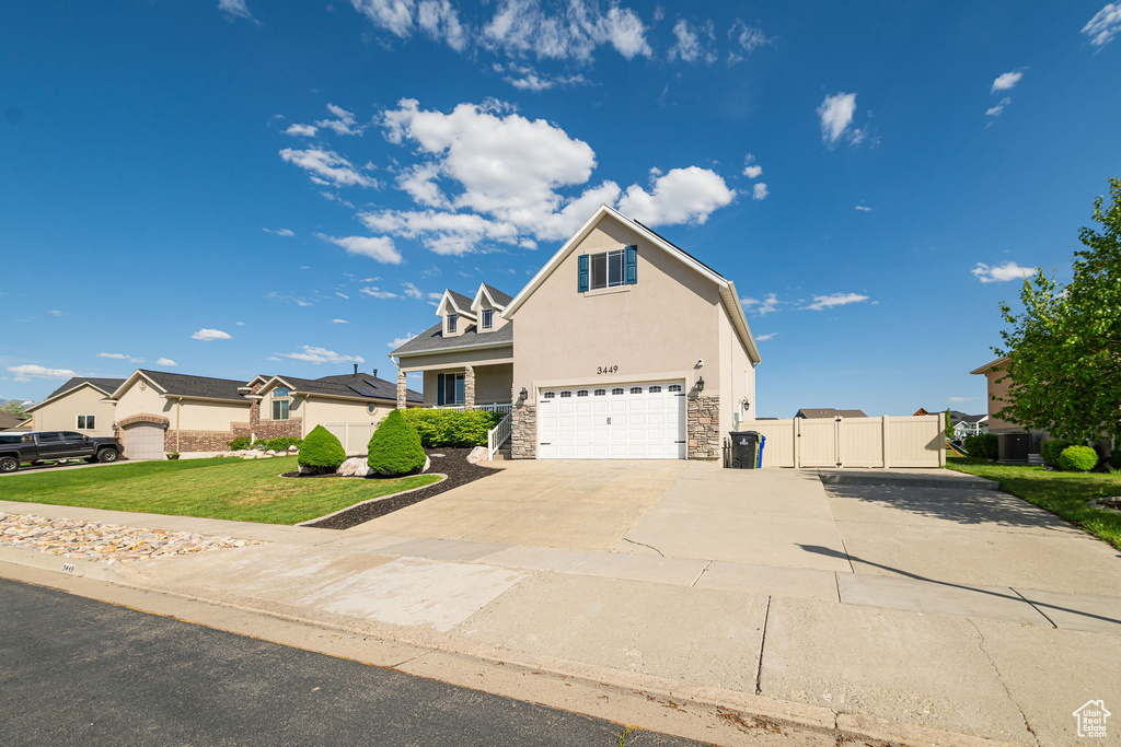 Traditional-style house with an attached garage, stone siding, driveway, a gate, and stucco siding