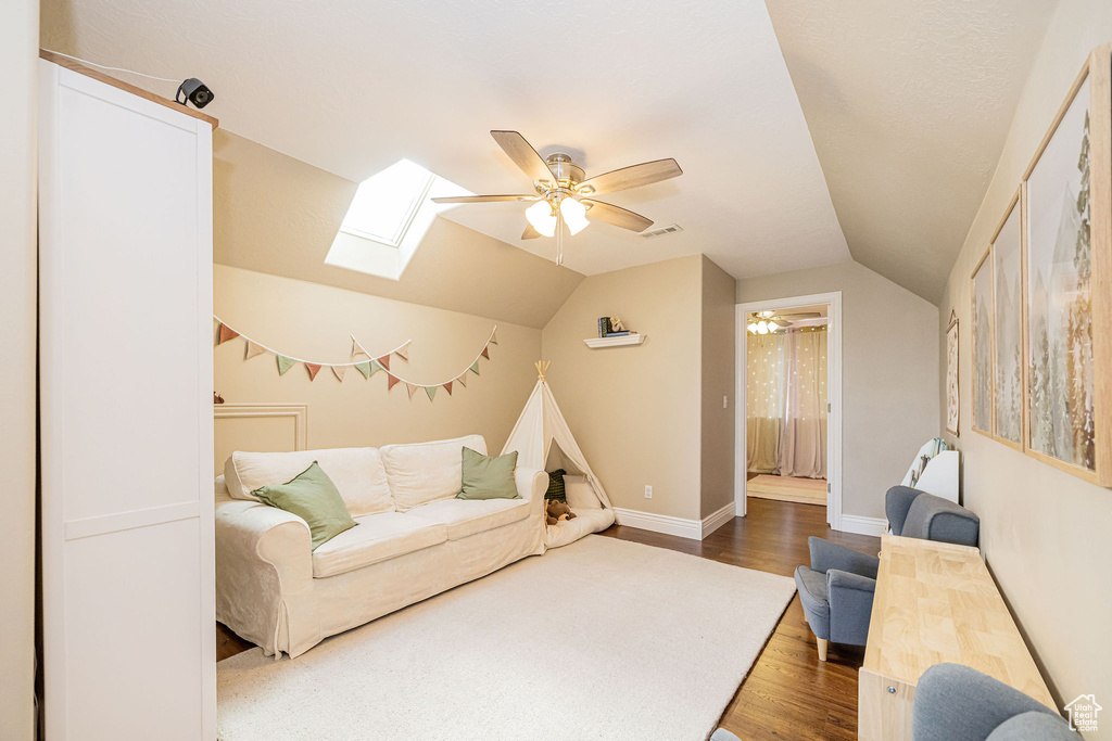 Living room featuring a skylight, ceiling fan, wood finished floors, vaulted ceiling, and baseboards