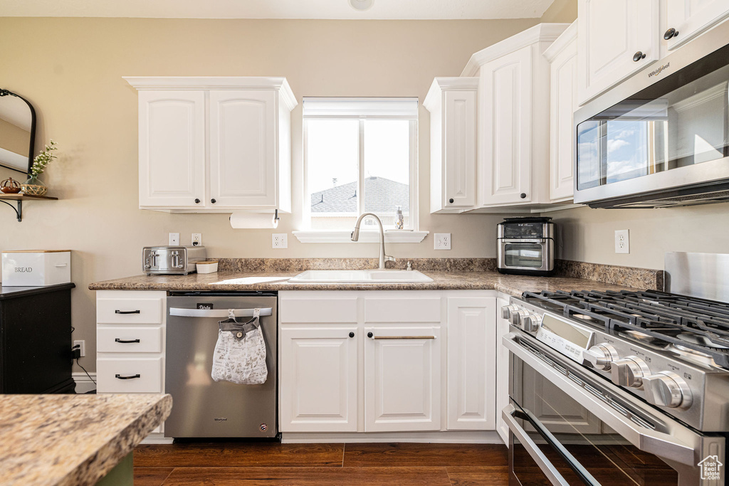 Kitchen with appliances with stainless steel finishes, a sink, white cabinetry, and dark wood-style floors