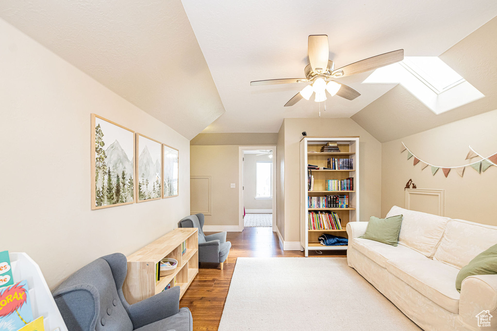 Living room featuring a skylight, ceiling fan, wood finished floors, baseboards, and lofted ceiling