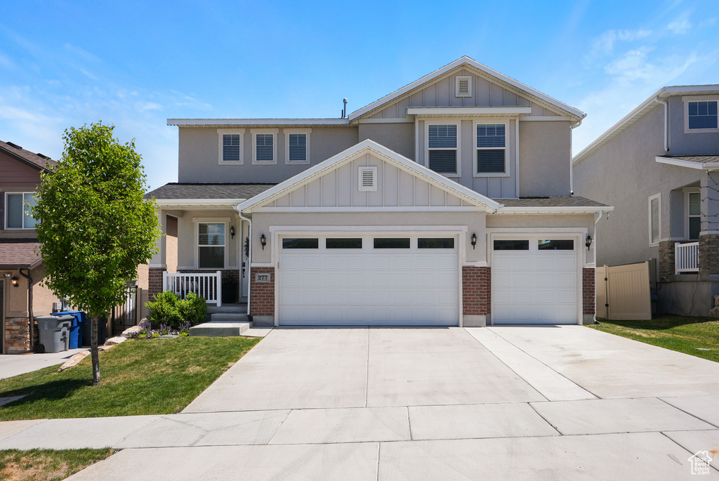 Craftsman-style home with board and batten siding, concrete driveway, brick siding, a front lawn, and an attached garage