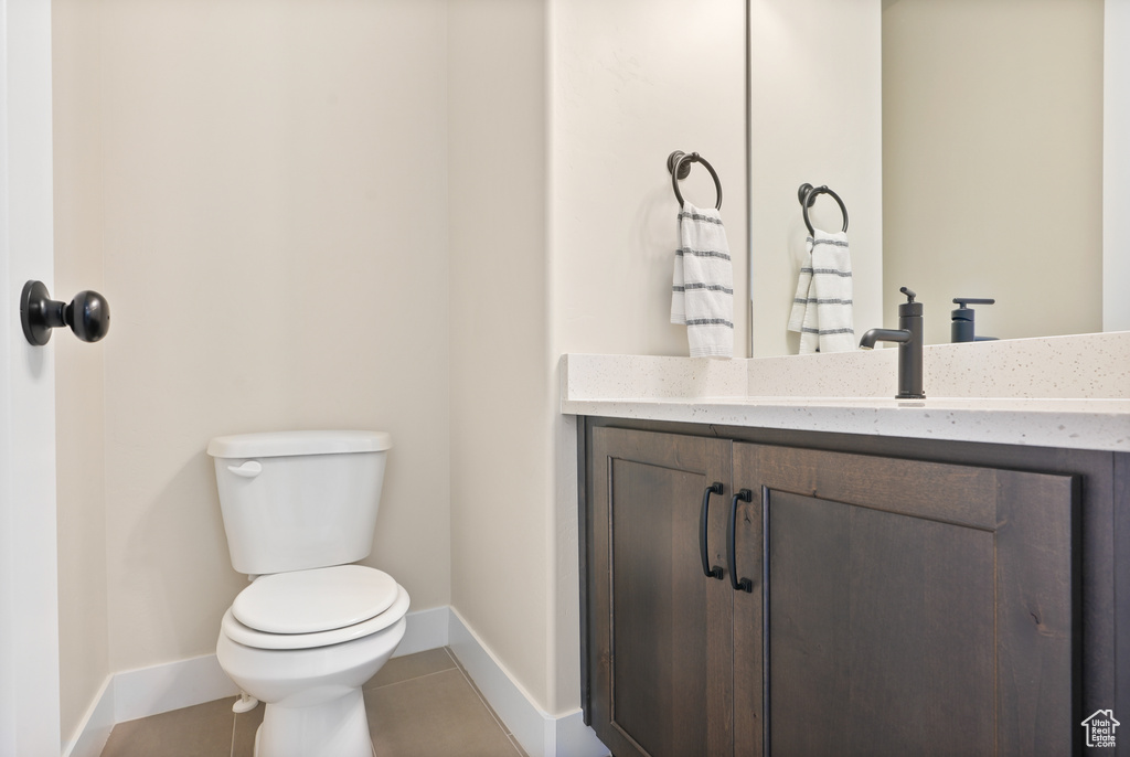 Half bath featuring baseboards, toilet, vanity, and tile patterned floors