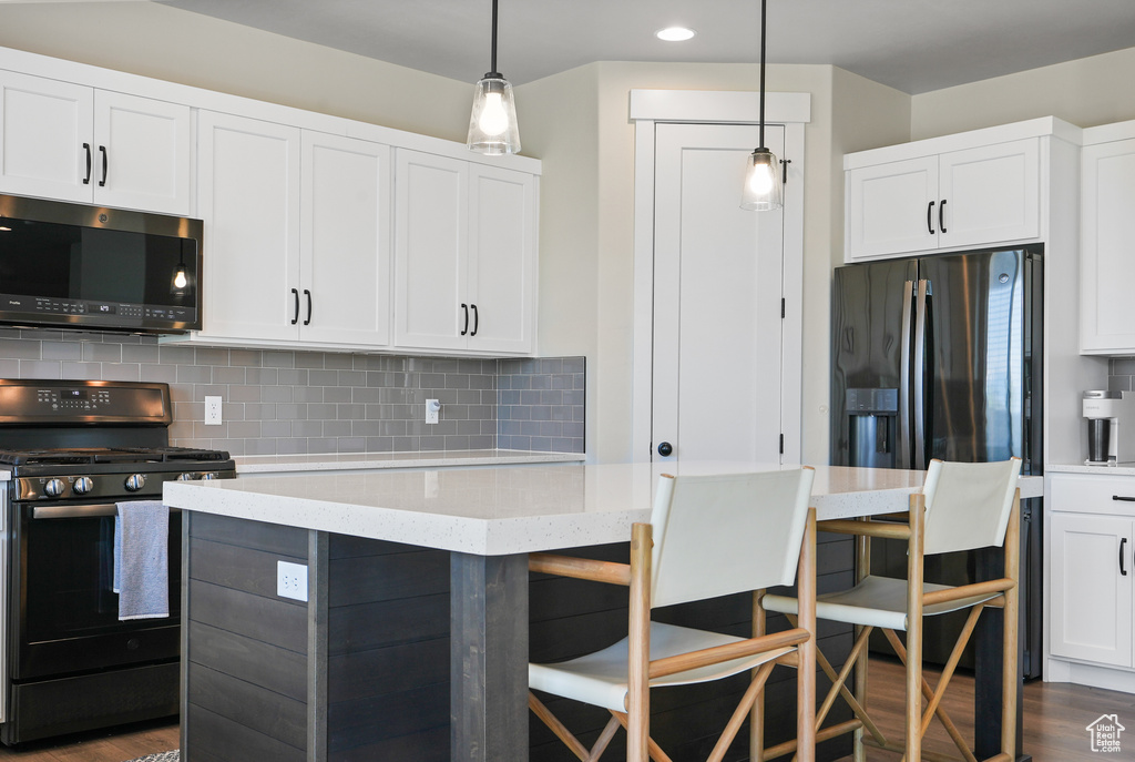 Kitchen with black range with gas cooktop, tasteful backsplash, a breakfast bar, white cabinetry, and dark wood finished floors