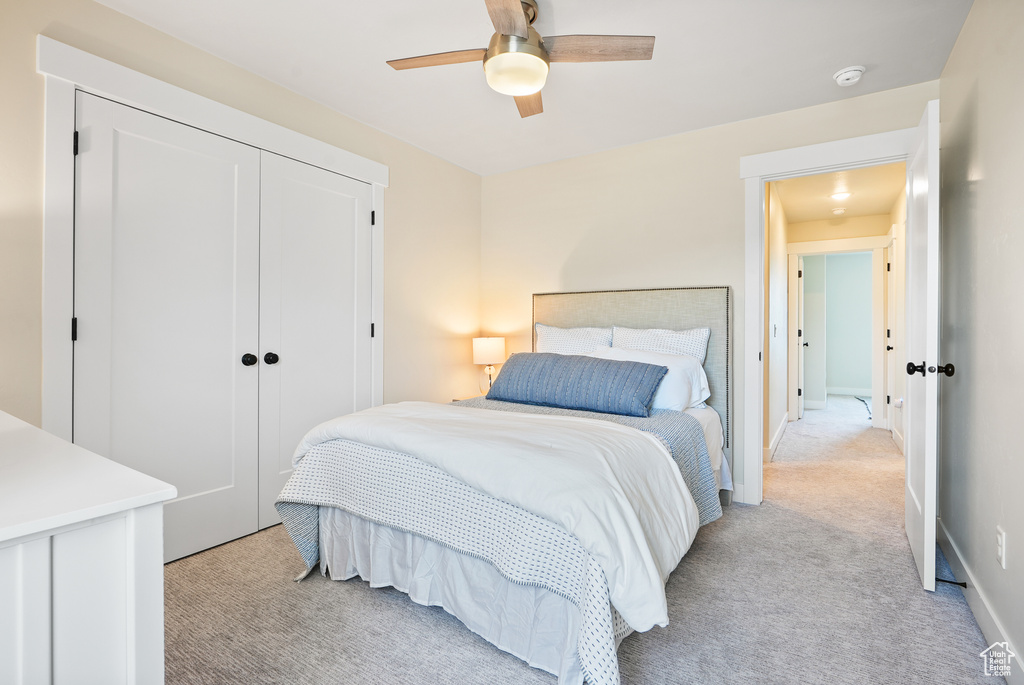 Bedroom with light colored carpet, a closet, and a ceiling fan