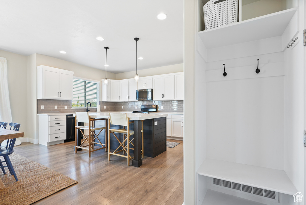 Kitchen featuring appliances with stainless steel finishes, a breakfast bar area, white cabinetry, backsplash, and recessed lighting