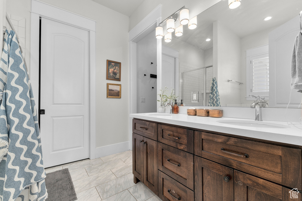 Bathroom with a stall shower, double vanity, marble look tile flooring, and baseboards