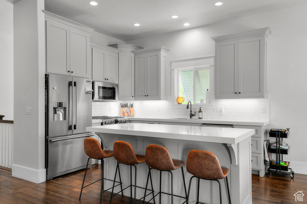Kitchen featuring appliances with stainless steel finishes, a sink, a kitchen breakfast bar, dark wood-style floors, and a center island