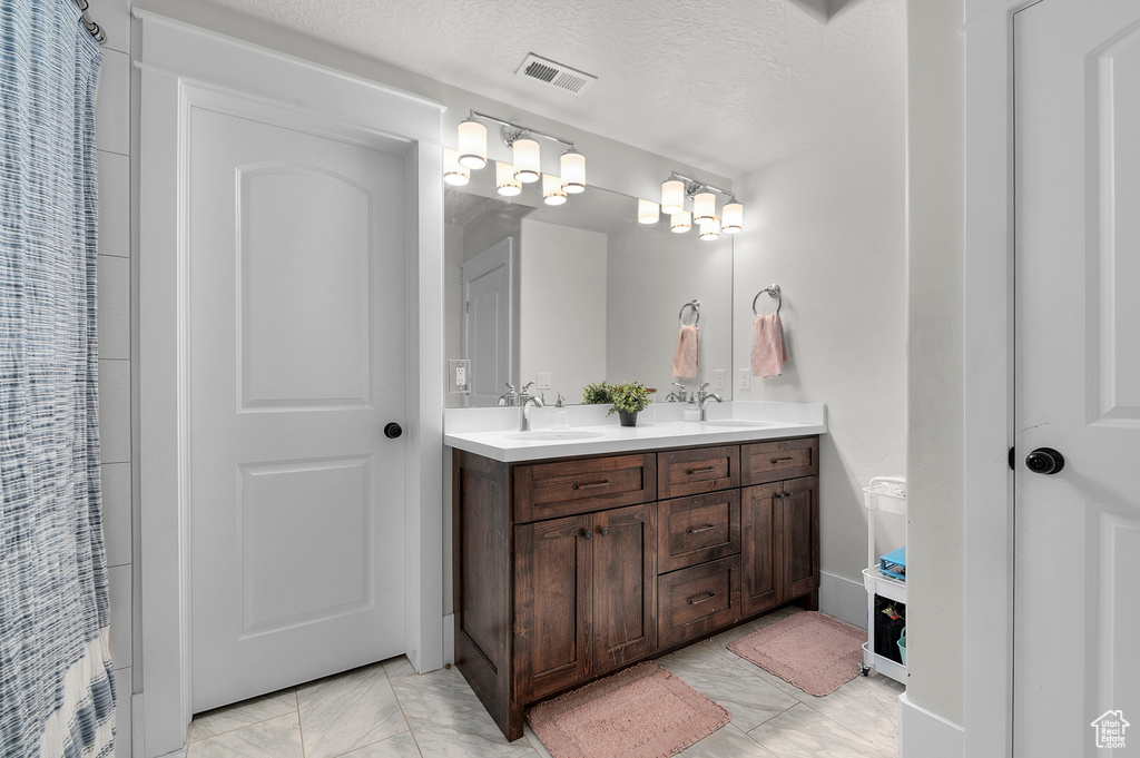 Full bath with double vanity, marble finish floors, and a textured ceiling
