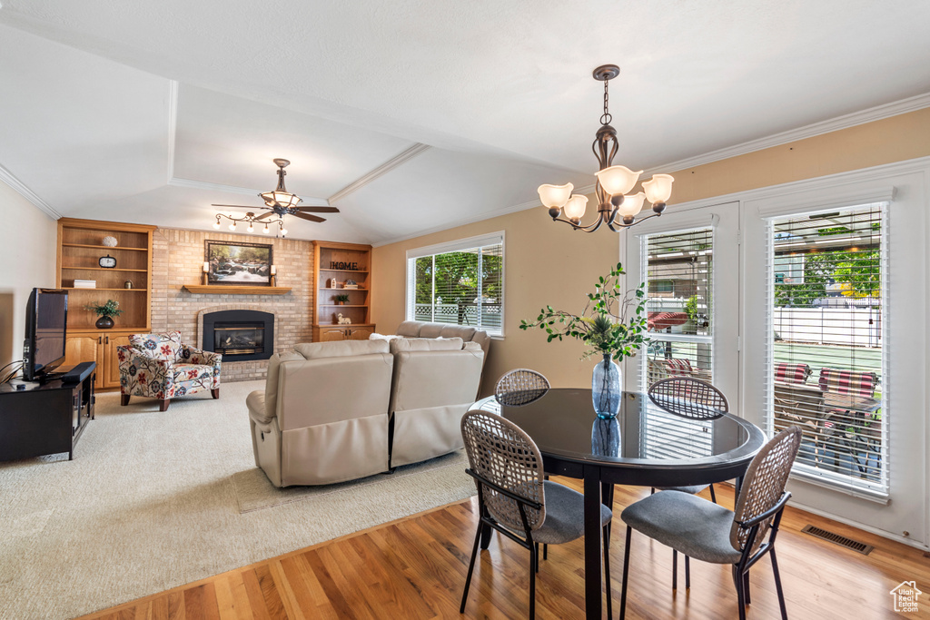Dining space featuring a ceiling fan, a chandelier, a fireplace, light wood-type flooring, and ornamental molding