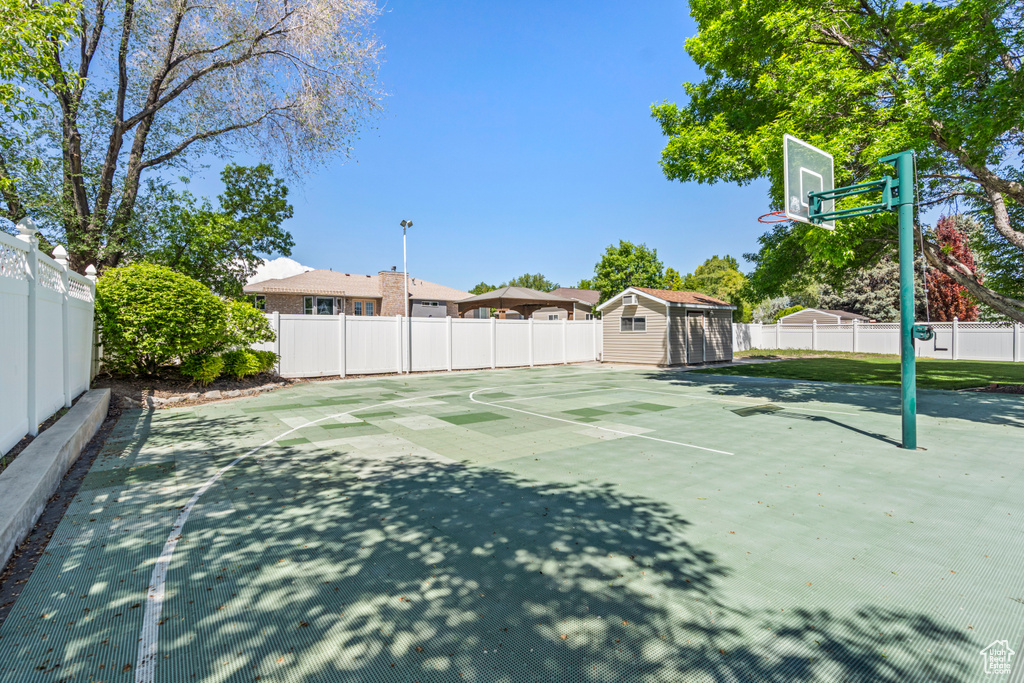 View of basketball court with basketball hoop, a shed, and fence