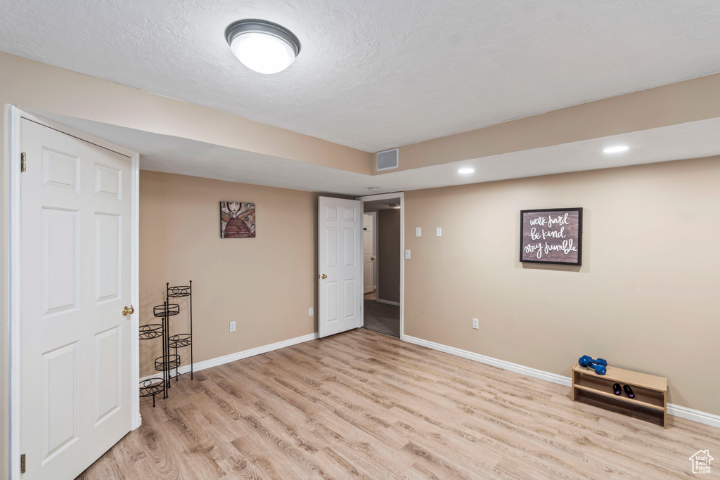 Finished basement featuring light wood-style flooring, baseboards, recessed lighting, and a textured ceiling