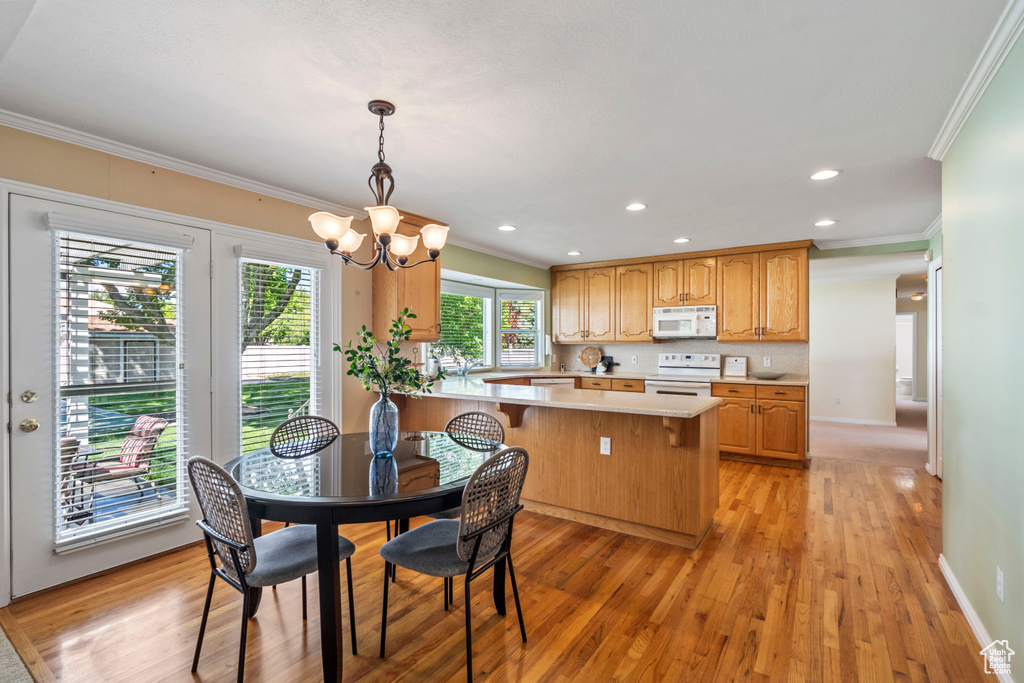 Kitchen featuring white appliances, ornamental molding, light countertops, light wood finished floors, and a chandelier