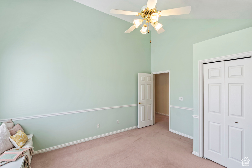 Unfurnished bedroom featuring light carpet, high vaulted ceiling, a closet, baseboards, and ceiling fan