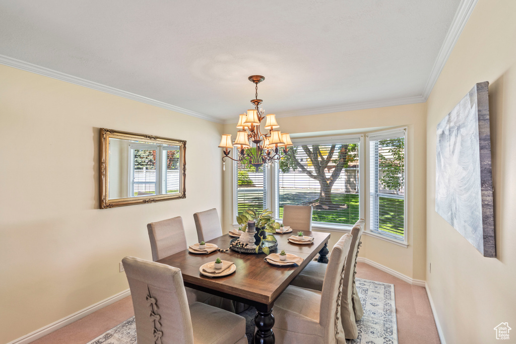 Dining space with a chandelier, light colored carpet, baseboards, and crown molding