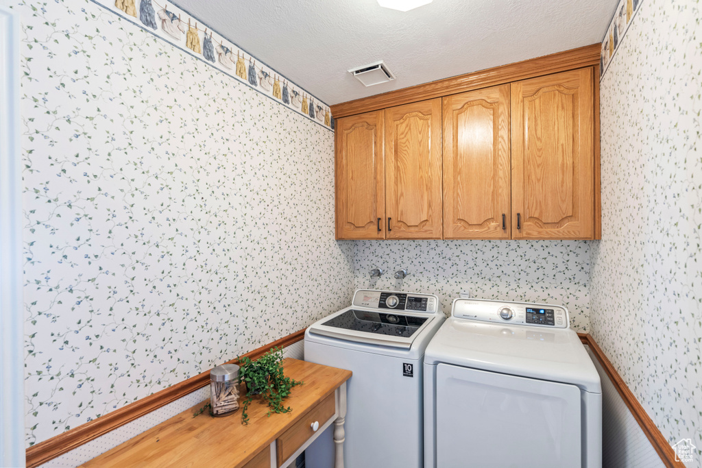 Laundry area featuring wallpapered walls, cabinet space, and washing machine and dryer