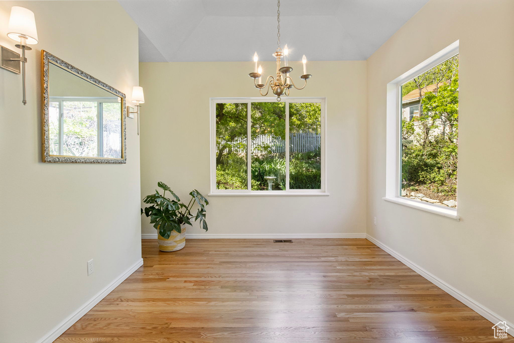 Unfurnished dining area featuring a chandelier, wood finished floors, lofted ceiling, and baseboards
