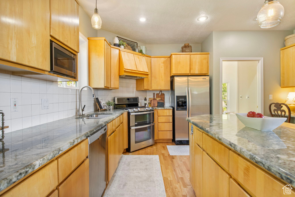 Kitchen with stainless steel appliances, a sink, light wood-style flooring, decorative backsplash, and dark stone countertops