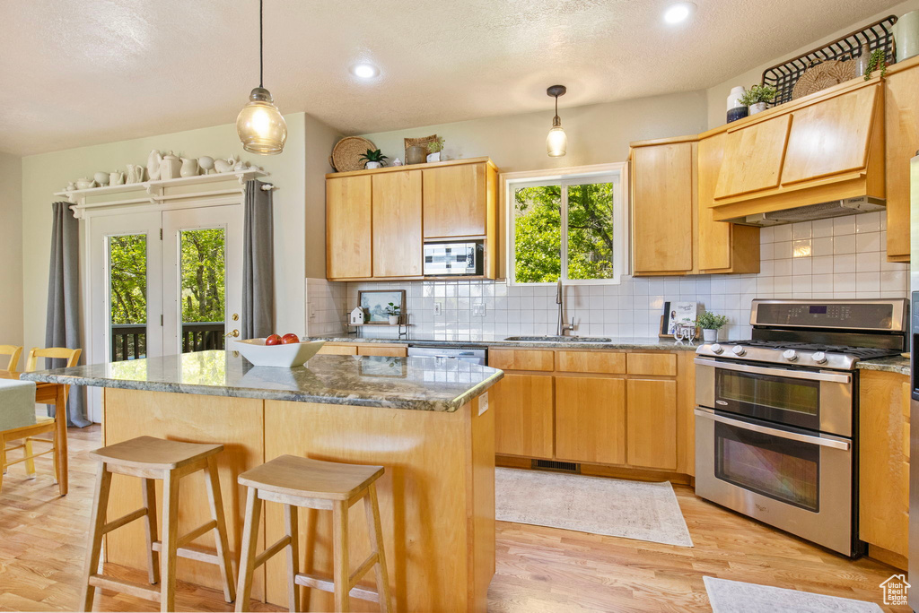 Kitchen with double oven range, a sink, decorative backsplash, light wood-type flooring, and built in microwave