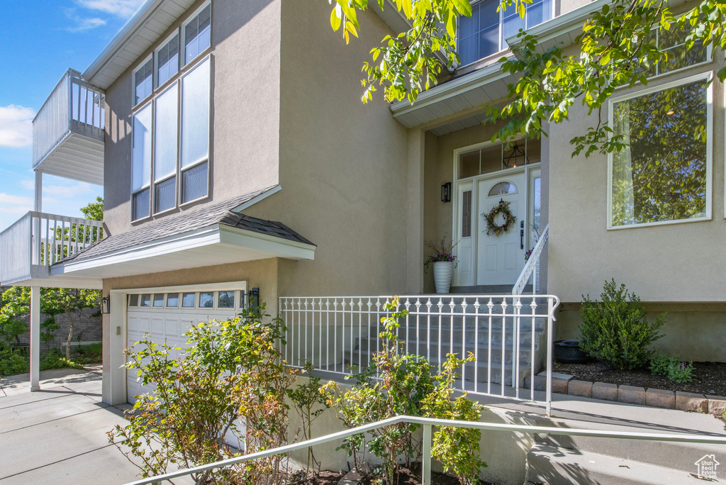 Property entrance with a garage, stucco siding, and a balcony