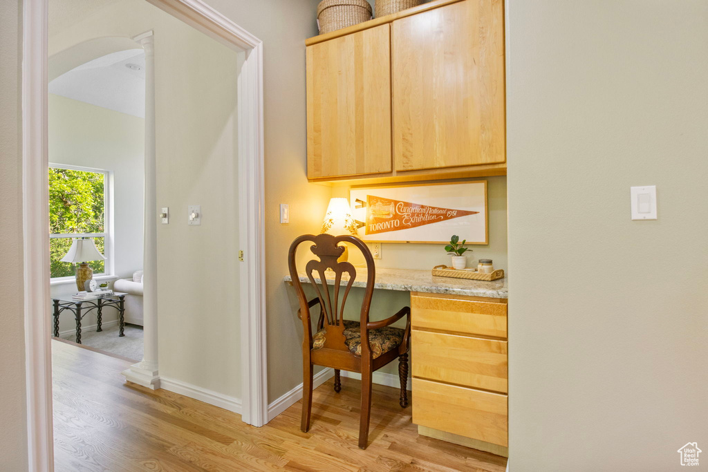 Hallway with light wood finished floors, baseboards, arched walkways, and a desk