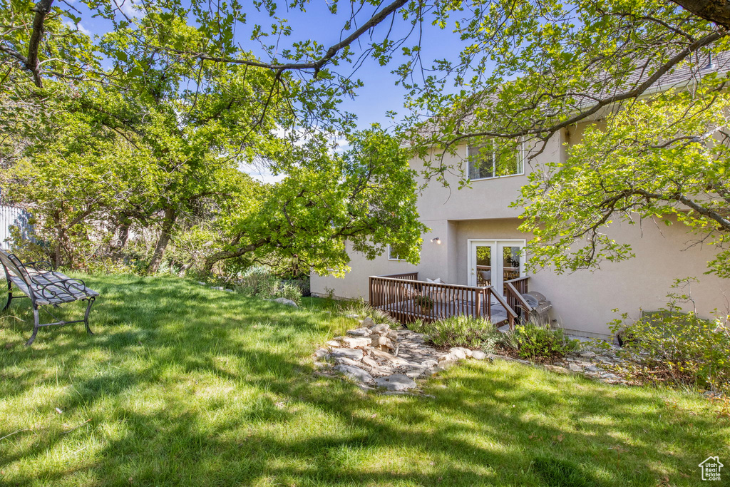 View of grassy yard featuring a wooden deck and french doors